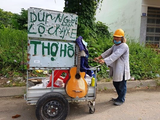 Ông Bùi Văn Thuận (45 tuổi, ngụ phường Mỹ Phước, TP.Long Xuyên) đẩy chiếc xe ba gác đã chuẩn bị sẵn đồ nghề, lọ mọ, quan sát tìm những ổ gà trên đường để vá - Ảnh: Tô Văn
